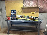 Full view of metal work table, pegboard backboard mounted on wall, assorted small tools and containers on table surface, and shelves above.