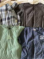 Four men's casual shirts including one plaid button-up and three graphic tees in black, green, navy blue, and mint.