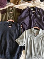 Close-up of various men's casual shirts including sweaters and polo shirts, showing material and brand details