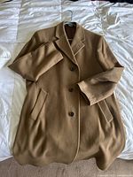 Camel-colored men's formal overcoat displayed on bed, single-breasted with three buttons and notch lapels.