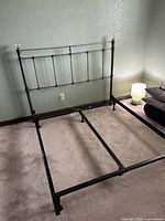 Metal black queen bed frame and headboard in a bedroom on carpeted floor, showing six supporting legs on the frame.