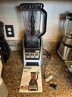 Full view of Ninja blender base, pitcher and power cord with owner's manual in front on countertop