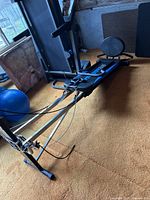 Full view of Total Gym XLS Pilates machine showing frame, sliding board, resistance cables with handles, and padded seat in a basement setting.
