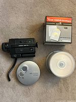 Chinon 313P XL video camera, Sony Walkman CD player, blank DVDs and DVD envelopes arranged on carpet.