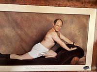 Photo of the framed Seinfeld poster featuring an unshaven man in white shorts on a chaise lounge, titled 'The Timeless Art of Seduction'