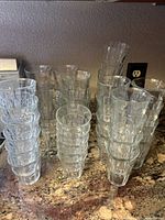 Multiple stacks of clear drinking glasses in various sizes placed on countertop next to peninsula wall outlet.
