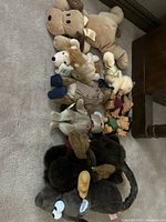Multiple small stuffed animals and character plush toys arranged on floor including moose, dog in clothing, elephant, and other assorted animals.