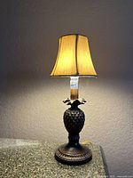 Image of the small tabletop lamp with bronze decorative base and cream fabric shade illuminated, showing design details and light output.