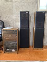 Two stacked speaker towers and a wooden media cabinet with glass door in basement setting