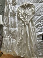 Photo of wedding dress laid flat showing front side, fabric texture, long sleeves, beaded high neckline, and part of the train