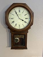 Full view of wooden Bulova wall clock showing clock face with Roman numerals and pendulum case labeled REGULATOR.