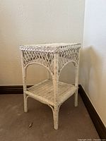 White vintage wicker side table in corner showing front view and lower shelf.