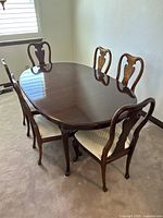 Full view of the polished dark wood oval dining table with six matching chairs featuring cream upholstered seats.