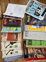 Photo of 15 various music books arranged on a wooden surface showing titles related to guitar method, drum book, and harp music.
