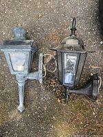Two vintage cast iron wall lamps placed on ground showing side and top views in natural light.