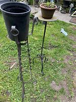 Two wrought iron plant stands on grass; one with a bucket, one with flat platform.