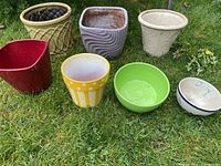 Overview of all seven porcelain pots placed on grass showing colors, shapes, and sizes.