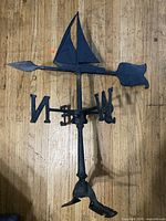 Full overview of the antique metal sailboat weathervane laid on a wood floor showing overall shape and size.