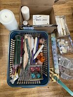 Full view of assorted candles in box and basket, large pillar candles, boxed white linen candles, and packs of small candles.