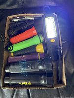 Box containing various flashlights of different sizes, colors and styles shown from above