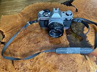 Front view of Canon AE-1 camera with lens and attached neck strap on wood surface