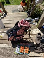Child’s pink and black golf bag with clubs and three packages of practice golf balls placed on wooden steps.