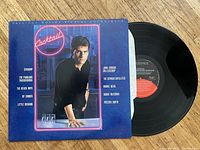 Vinyl record partially out of its cover showing cover art with actor Tom Cruise and track list including artists like Starship, The Fabulous Thunderbirds, The Beach Boys, among others.