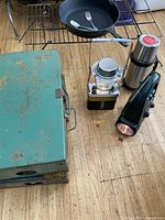 All items together including cast iron pan with utensils, battery lantern, thermos, flashlight, and green metal radio box on wooden floor