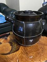 Front and side view of the black ceramic fermentation pot with lid on a wooden table, showing the body shape and handles.