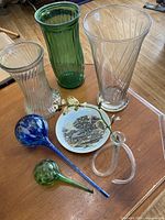 Photo showing all items including four glass vases, two watering vessels, and decorative plate on wooden table.
