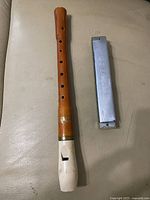 Metal harmonica and wooden recorder laid side by side on a light surface.