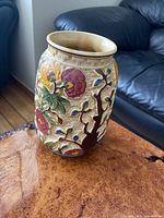 Ceramic vase with embossed tree, flower designs on beige base on wooden surface near sofa