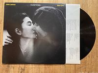 Photo of album cover showing John Lennon and Yoko Ono kissing, partially showing the black vinyl record and printed inner sleeve.