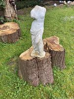 Photo of classical style female torso garden statue placed on a wooden stump outdoors.