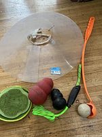 Full view of the pet cone collar, Kong chew toys, dog leash, orange fetch stick with ball, and green rubber bowl on wooden floor