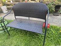 Outdoor black woven seat and backrest metal bench without cushion on grassy area.