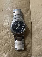 Men's Mazda watch face and bracelet laid flat on beige leather surface, showing details of dial and metal links.