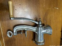 Side view of cast metal manual meat grinder with wooden handle and clamp.
