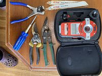 All items arranged on wooden surface, visible tools include screwdrivers, crimpers, snips, blades, and orange measuring device in case.