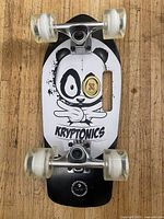 Top view showing the skateboard deck with a panda graphic and the Kryptonics brand name on a wooden floor.