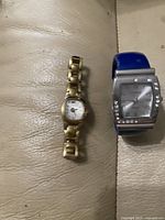 Two women's watches laid out side by side on a beige leather surface, showing the full watches and details of the faces and bands.