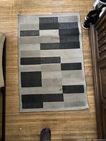 Top-down view of rectangular grey patterned rug mat with abstract geometric blocks in varying greys and black on a lighter grey base.