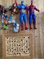 Photo showing the assortment of plastic action figures and animal figures arranged on floor, with wooden labyrinth game below.