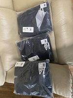 Three pairs of Umbro black sweatpants, brand new and sealed in plastic on a beige couch.