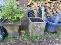 Three outdoor planters arranged in a row: two concrete-like square planters on the left, and a round blue plastic planter with a blue owl inside on the right.