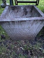Close-up of the front side of the square planter showing the floral design and weathered surface.