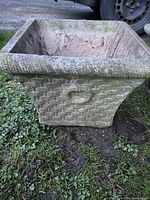 Photo of vintage concrete planter showing side with basket weave and wreath textured design and weathered surface.