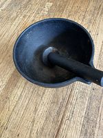 Close-up side view of the cast iron mortar bowl with pestle inside, showing the dark seasoned surface and rounded shape.
