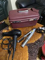 Vintage burgundy travel case with black Revlon hair dryer and curling iron brush laid out on textured surface