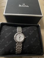 Front view of Bulova watch on black cushion inside branded box